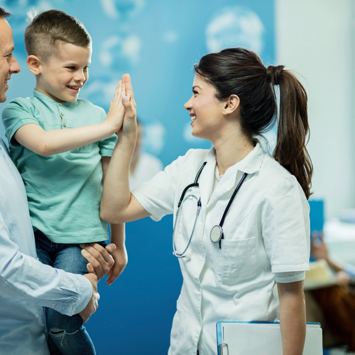 Happy female doctor giving high fie to a little boy who came with father at hospital.